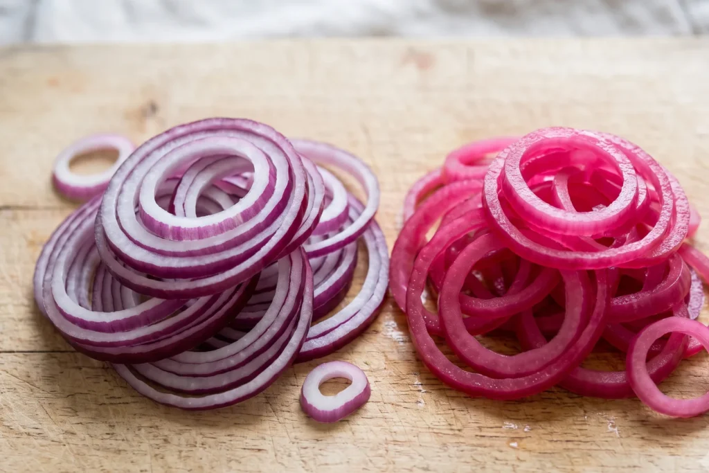 Links frisch geschnittene violett-weiße rohe Zwiebelringe, rechts durchgezogene, leuchtend pinke eingelegte Ringe im Vergleich