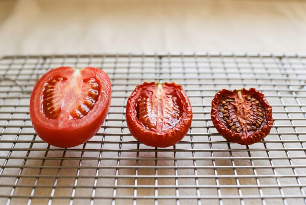 Drei Tomatenhälften nebeneinander: frisch, halb getrocknet und fertig ledrig getrocknet