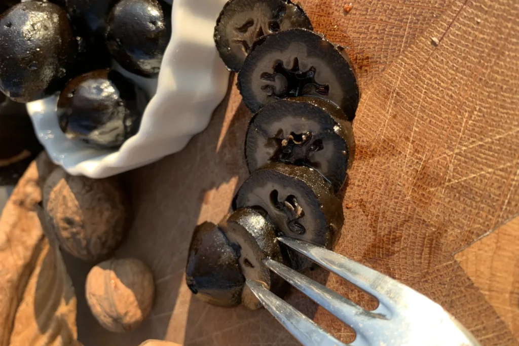 Aufgeschnittene schwarze Nüsse in einer Reihe mit sichtbarem Kernmuster, daneben eine Schale mit ganzen schwarzen Nüssen