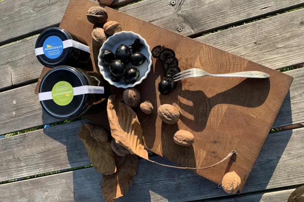 Holzbrett mit zwei etikettierten Gläsern, verstreuten Walnüssen und einer Schale voll ganzer und aufgeschnittener schwarzer Nüsse