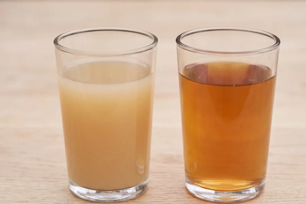 Ein Glas hellen, trüben Presssaft neben einem Glas dunkleren Dampfsaft auf gleichem Hintergrund