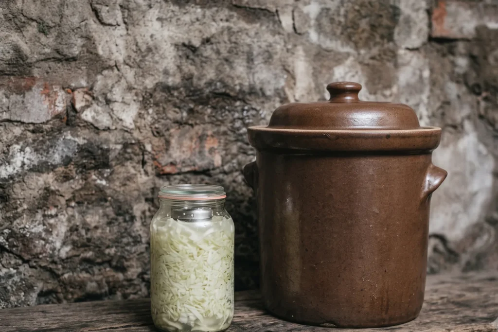 Kleines Ein-Liter-Fermentierglas neben einem deutlich größeren Steinzeug-Gärtopf