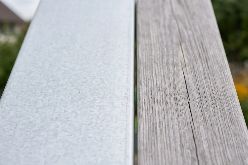 Verzinkte Stahlwand und verwitterte Holzbohle grenzen im Detail aneinander